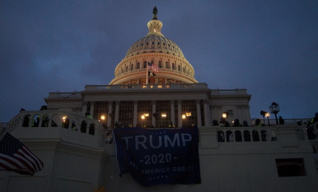 Trump 2020 flag draped over balcony with White House behind in the background