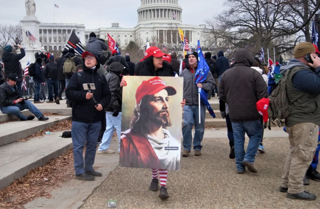 Women holding sign of Jesus wearing a MAGA hat in front of Capitol of January 6, 2021